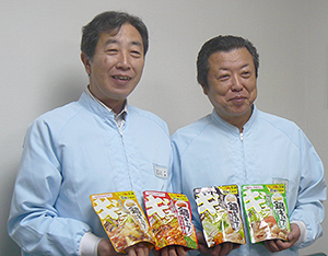 工場で生産した新品種とリニューアル品を手にとる石川格社長（左）と清水正男取締役