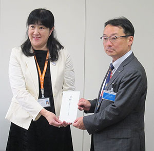 東京都福祉保健局の松川桂子次長（左）にアイスの寄贈目録を手渡す山本哲嗣理事長