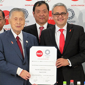 締結書を持つホルヘ・ガルドゥニョ社長（右）と森喜朗東京2020組織委員会会長。後列左は吉松民雄コカ・コーラボトラーズジャパン社長