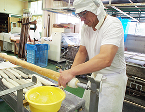 3回巻を作る宮村孝社長、長さ2mの金属棒に生地を巻き付けて繰り返し焼き上げる